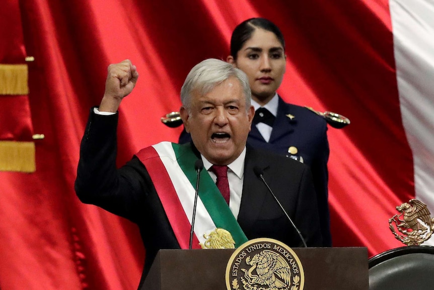 Mexico's new President Andres Manuel Lopez Obrador holds his hand in a fist and gestures with Mexican flag in background.