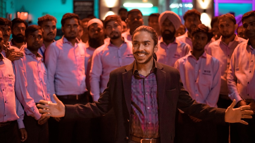 A still from the film The White Tiger with a young man in a suit (Adarsh Gourav) standing in front of a tech business