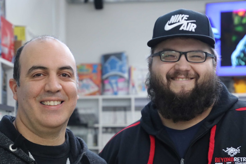 Two men, one balding the other with beard glasses and a cap, smile for a photo.