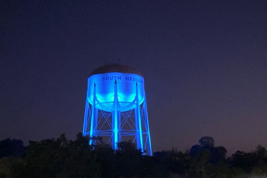 A large water tower is lit up in blue light from beneath, photographed at night.