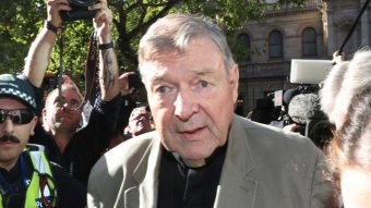 Cardinal George Pell walks into court, surrounded by police and media.