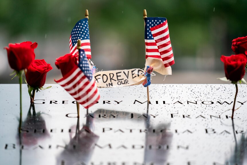Red flowers, US flag and 'forever in our hearts' sign sit on marble memorial stone