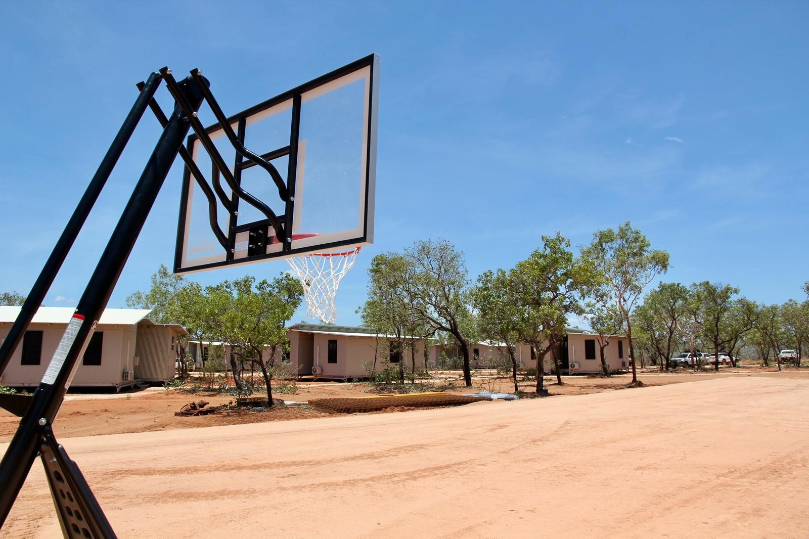 Un aro de baloncesto en un terreno polvoriento cerca de algunos pequeños edificios en el interior.