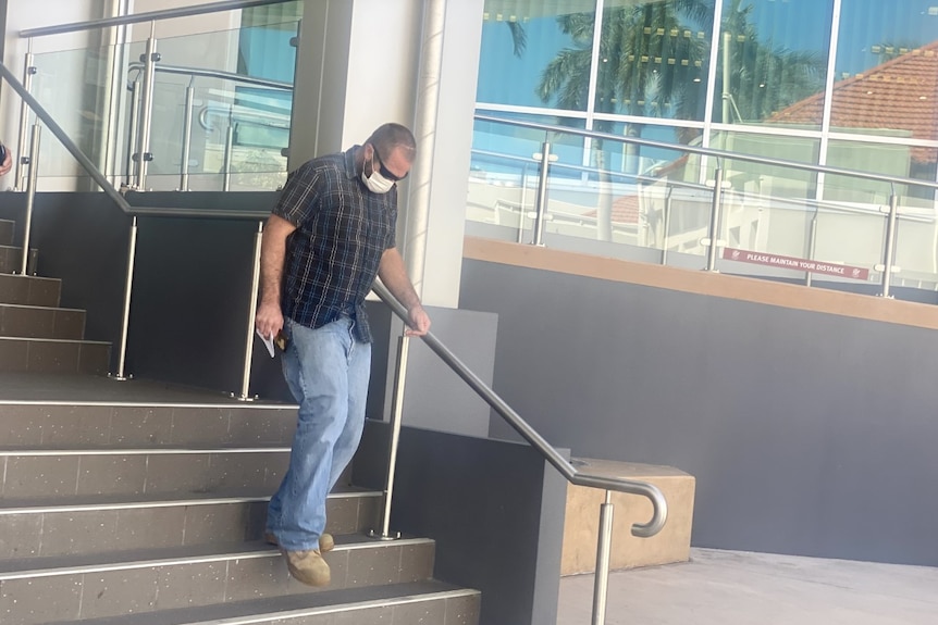 A man in a mask and sunglasses walks out of a court building.