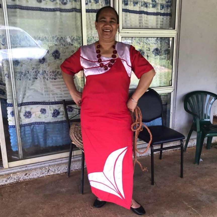 A woman in a red dress stands and smiles with her hands on her hips.