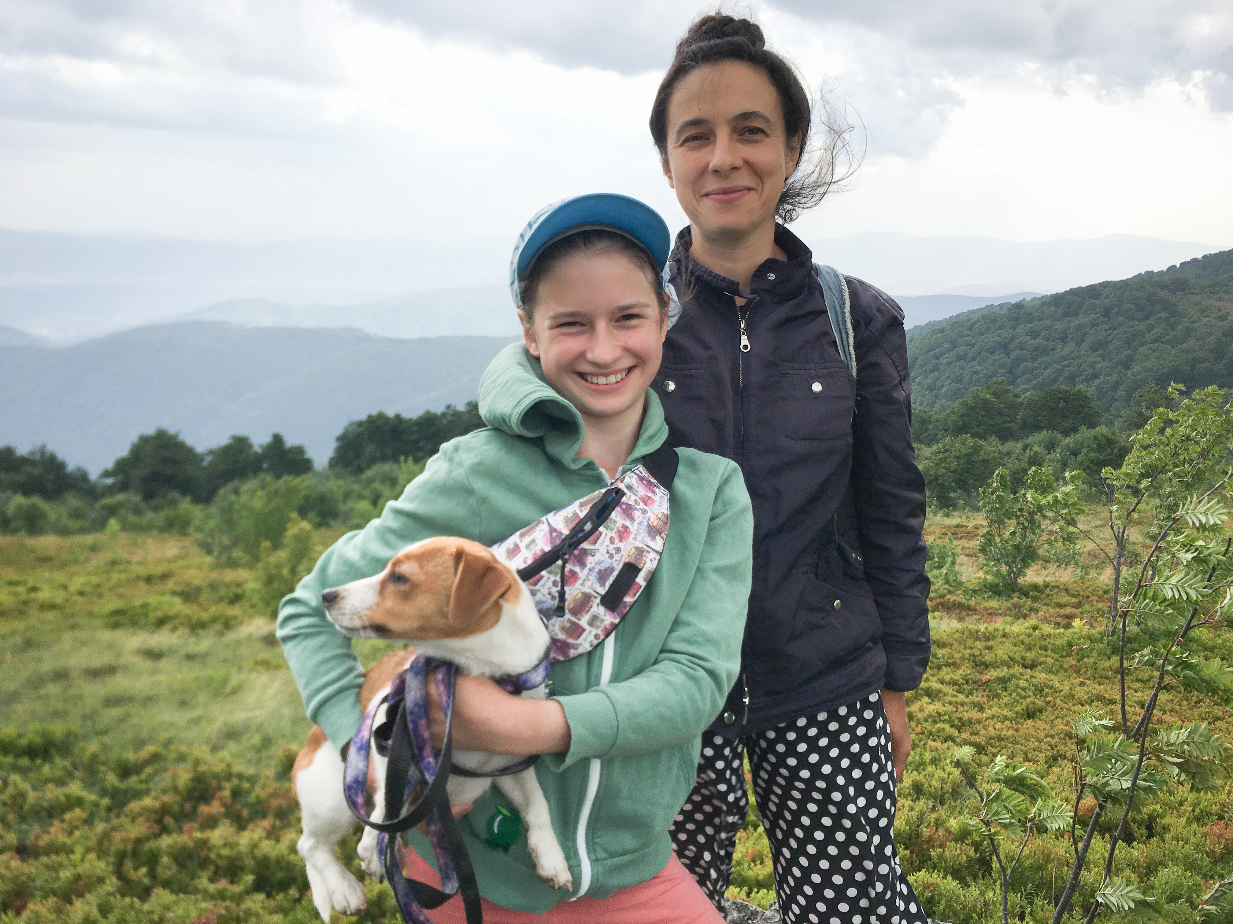 A mum and her daughter holding a dog with hills in the background