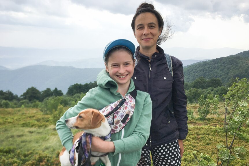 A mum and her daughter holding a dog with hills in the background