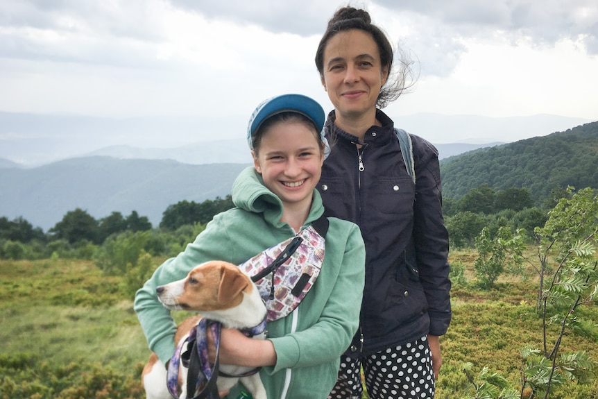 A mum and her daughter holding a dog with hills in the background