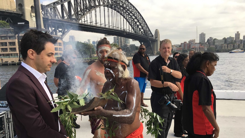 Aboriginal elder Uncle Max Eulo leads a smoking ceremony and holds the leaves in front of John Foreman in Circular Quay.