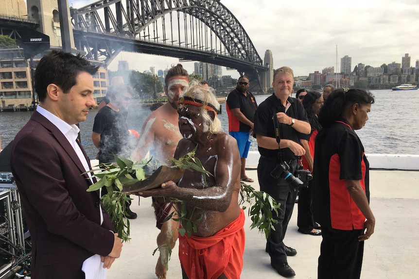 Aboriginal elder Uncle Max Eulo leads a smoking ceremony and holds the leaves in front of John Foreman in Circular Quay.