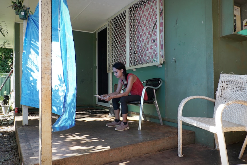 Caitlyn Roe sits on her phone outside her home.