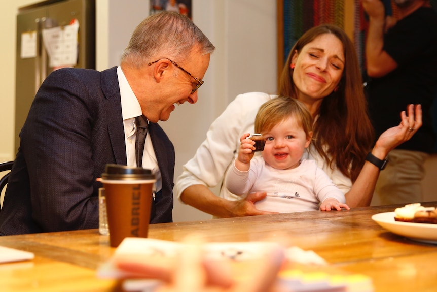Anthony Albanese laughs alongside woman as child holds up a cupcake.
