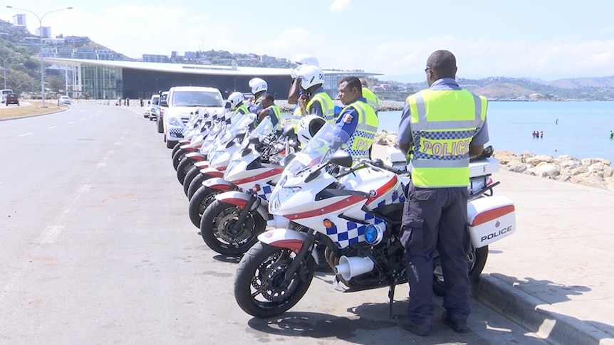 Police in PNG wearing high-visibility vests and standing with motorbikes.