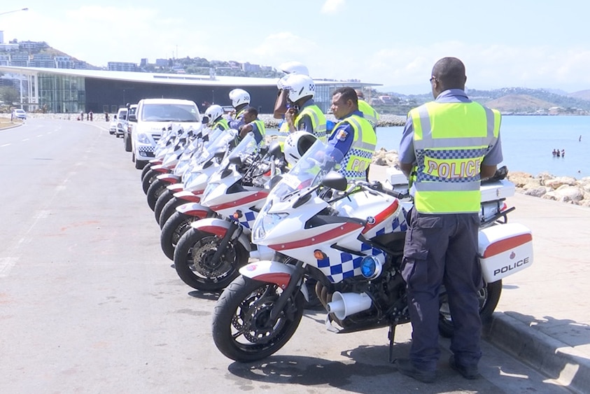 Police in PNG wearing high-visibility vests and standing with motorbikes.