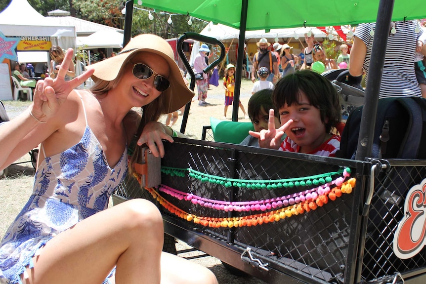 Woman in sundress, sunglasses, sunhat with two children in buggy