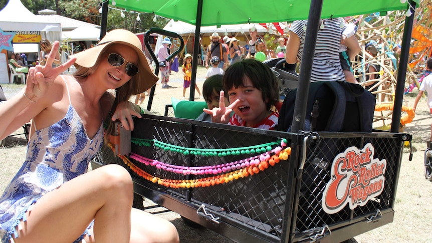 Woman in sundress, sunglasses, sunhat with two children in buggy