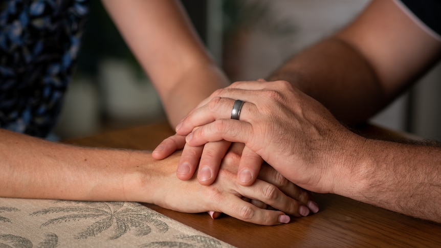 A Caucasian couple's hands grasp each other