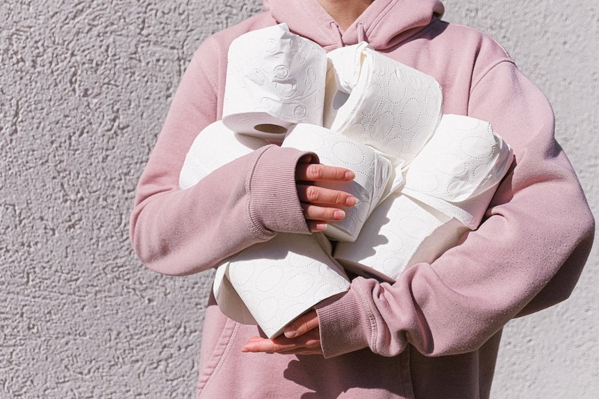A woman in a pink jumper holds a bunch of toilet paper rolls