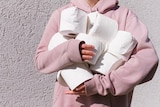 A woman in a pink jumper holds a bunch of toilet paper rolls