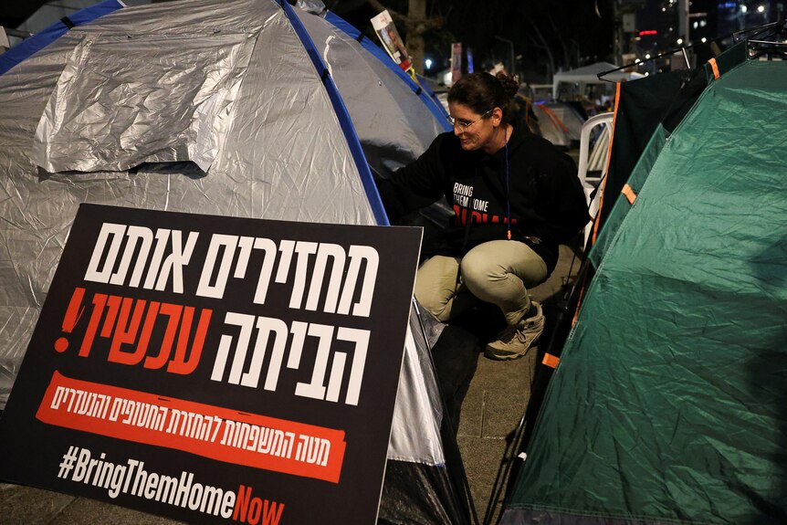 Woman sits next to tent and sign in hebrew 