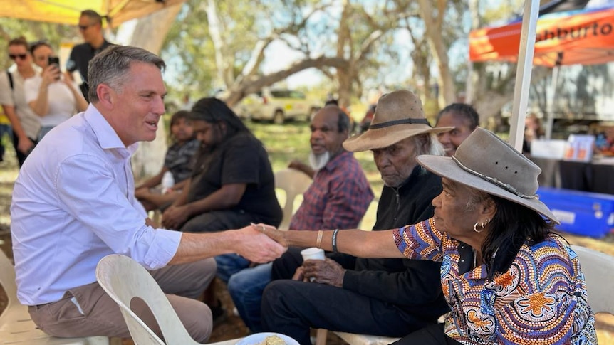 A man in a blue shirt speaks with older Indigenous women.