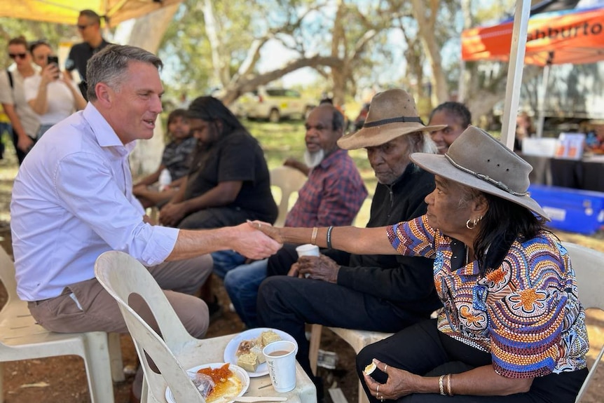 A man in a blue shirt speaks with older Indigenous women