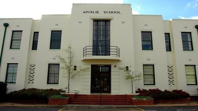 An old cream building with the words "Ainslie School" in black above the entrance.