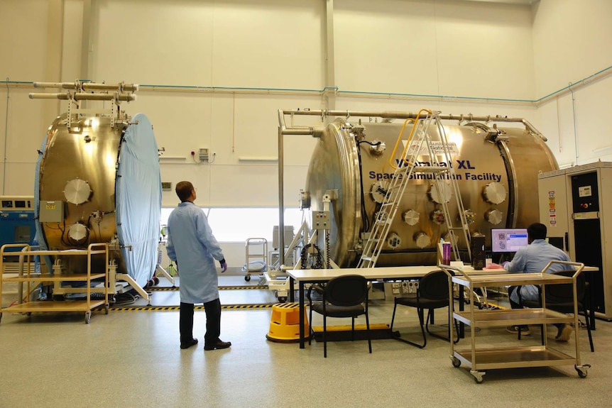 A man stands with his back to the camera looking at up at a large space simulation tank.