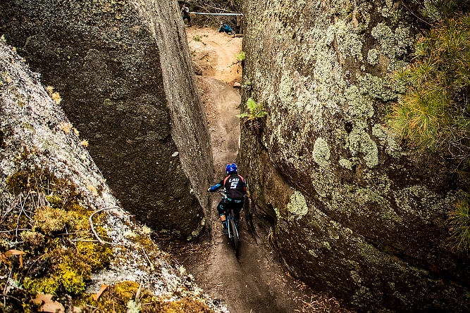 A bike rider goes between two large lichen-covered boulders.