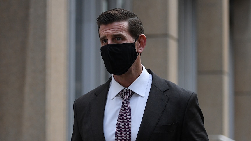 A man dressed in a suit and wearing a face mask walks past the camera. 