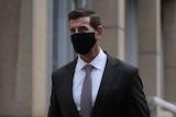 A man dressed in a suit and wearing a face mask walks past the camera. 