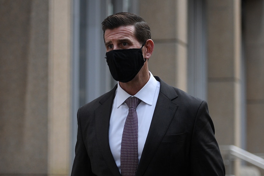 A man dressed in a suit and wearing a face mask walks past the camera. 
