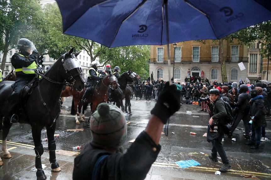 Mounted police face a group of protesters in the rain