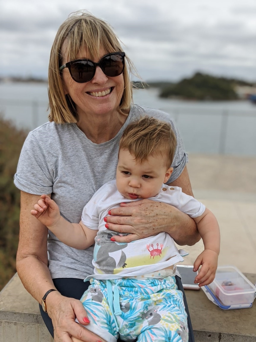 Robyn Hamblin nurses her young grandson under an overcast sky with a beach in the background