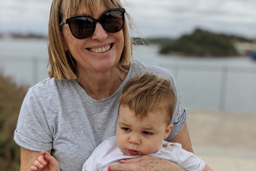 Robyn Hamblin nurses her young grandson under an overcast sky with a beach in the background