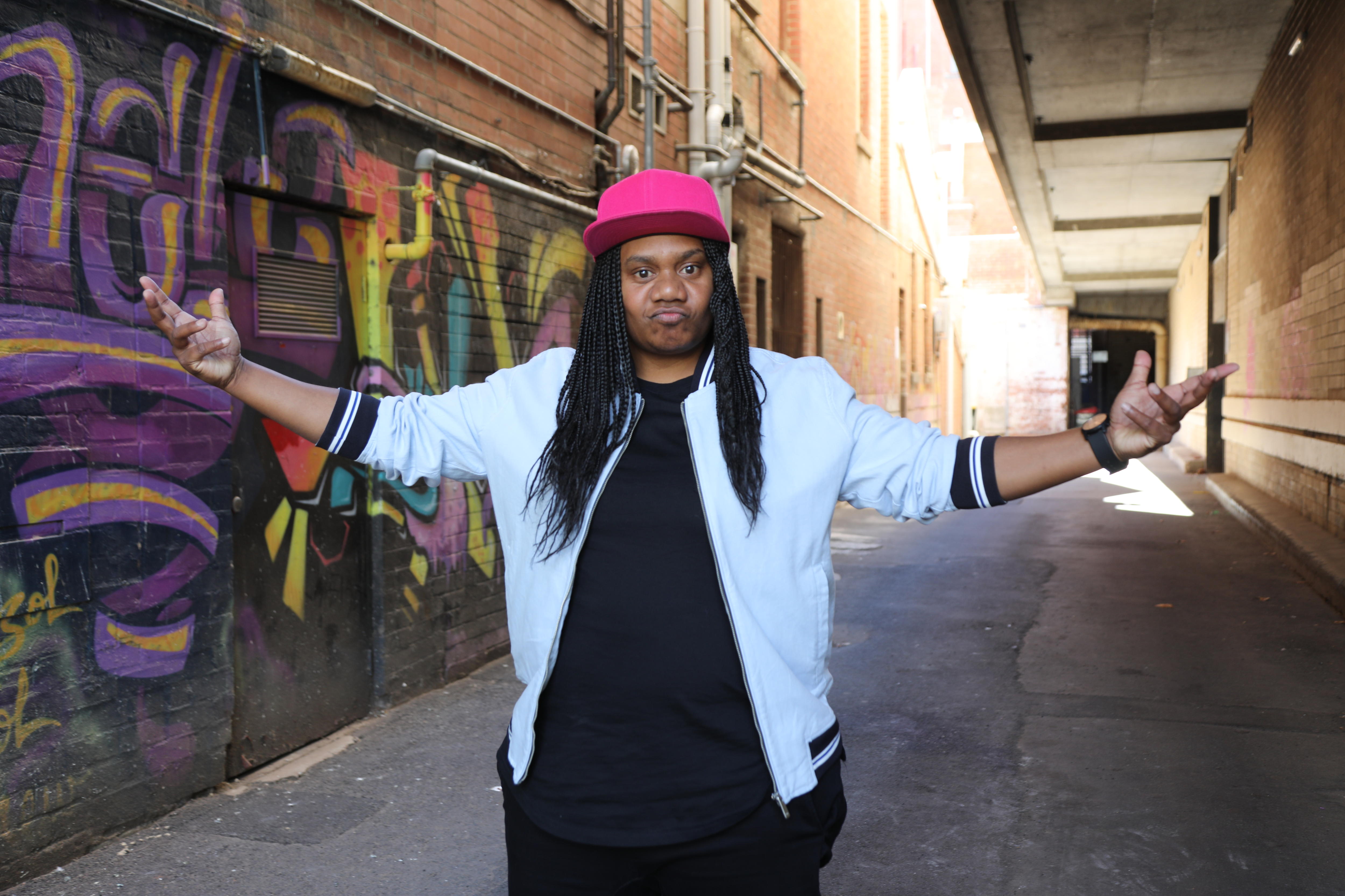 A man with dark skin and braids stood on the street, arms wide open.