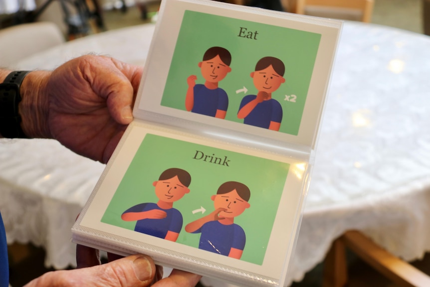 Someone holds a small book of hand signs, indicating signs for eat and drink.