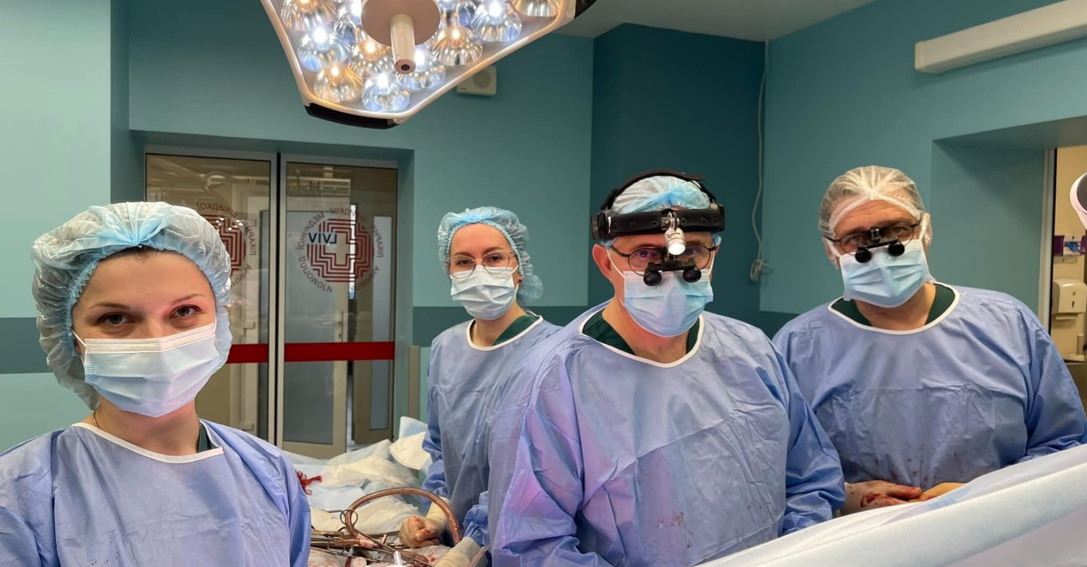 Cuatro cirujanos, dos hombres y dos mujeres, miran a la cámara con mascarillas y batas durante la operación. 