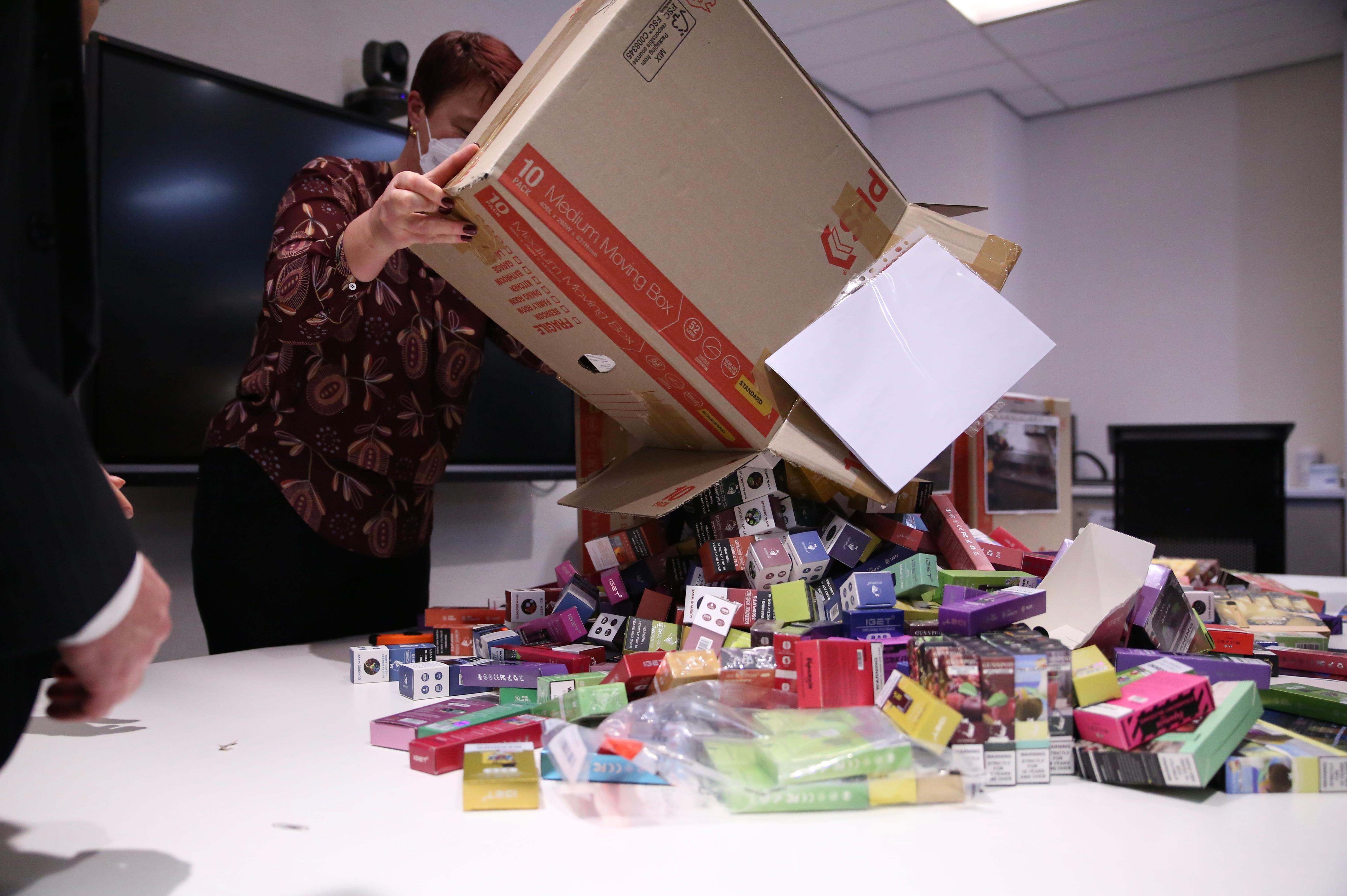 A cardboard box of vapes being tipped out on a white table