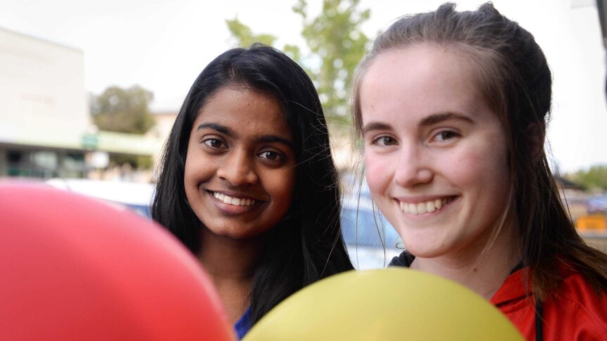 Two teenage girls smiling in front of coloured balloons.