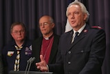 A man in a Salvation Army uniform speaks at a lectern. Behind him are two other men, in bishop's robes and a Scout's uniform.