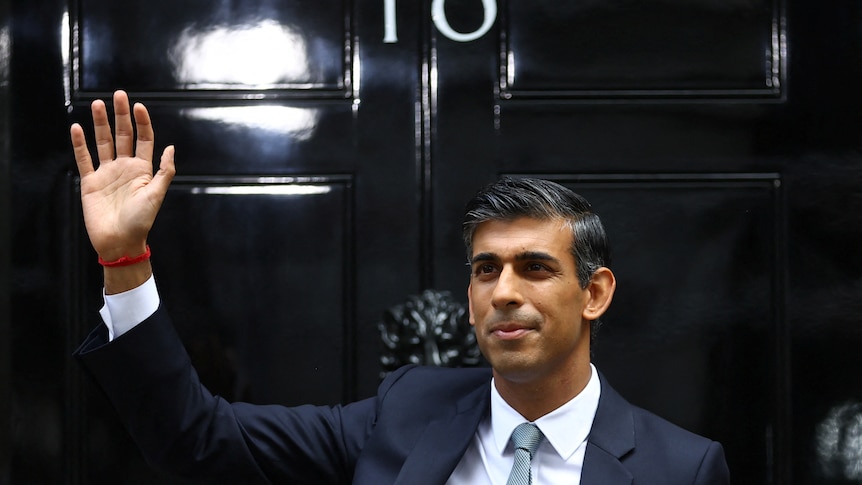 sunak in blue suit and tie waves out the front of the shiny black number 10 door