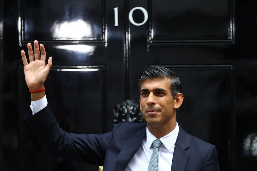 sunak in blue suit and tie waves out the front of the shiny black number 10 door