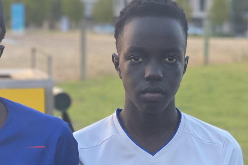 Teenage boy Atem Kuany stands wearing football jersey