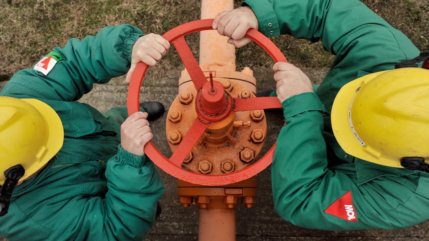 Engineers wearing green body suits turn the valve of a gas pipe