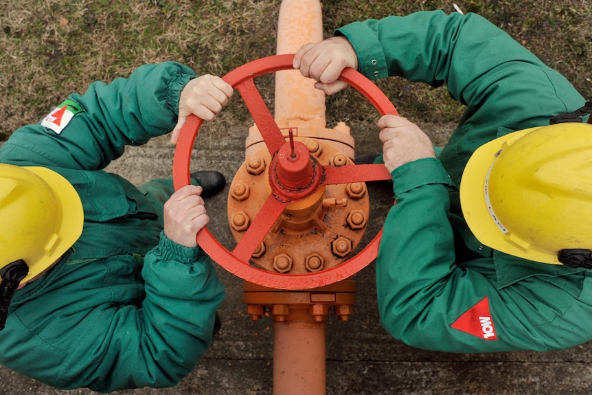 Engineers wearing green body suits turn the valve of a gas pipe