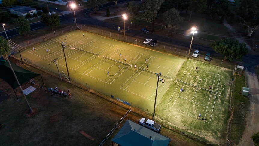 Aerial shot of five synthetic grass tennis courts at night.