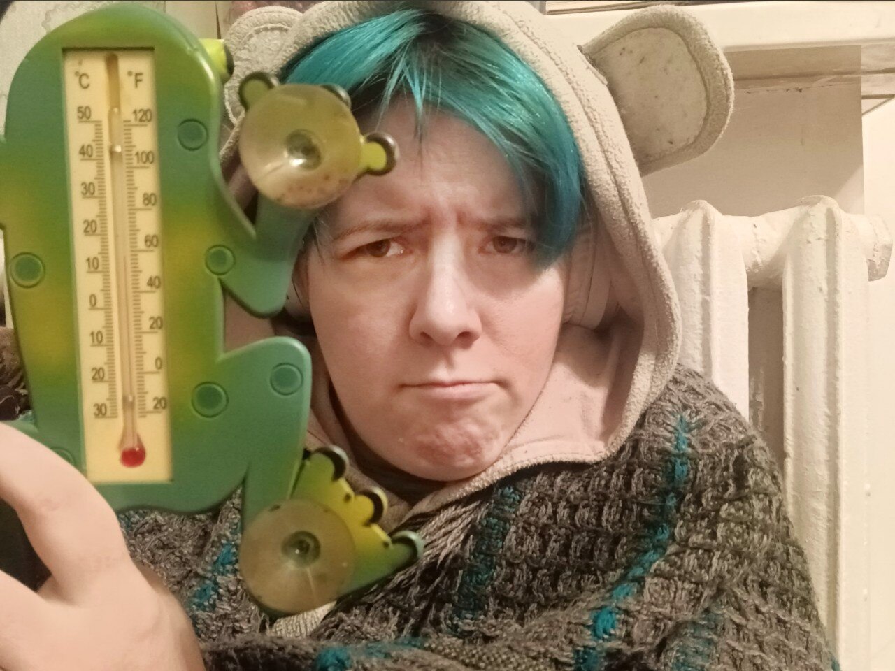 A man holding a thermometer and dressed in warm clothes frowns at the camera