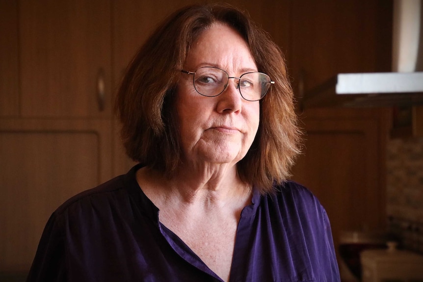 A woman wearing glasses and a purple shirt looks at the camera