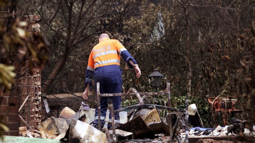 A policeman and forensics officer looks over a house where five people died at Kinglake